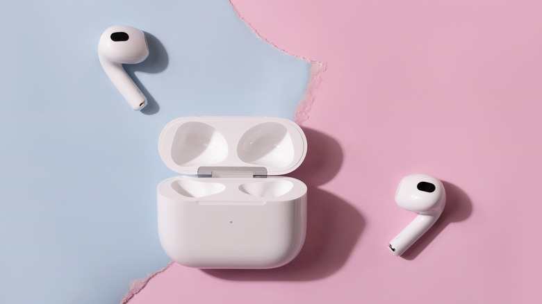 Apple AirPods and their charging case against a blue and pink backdrop.
