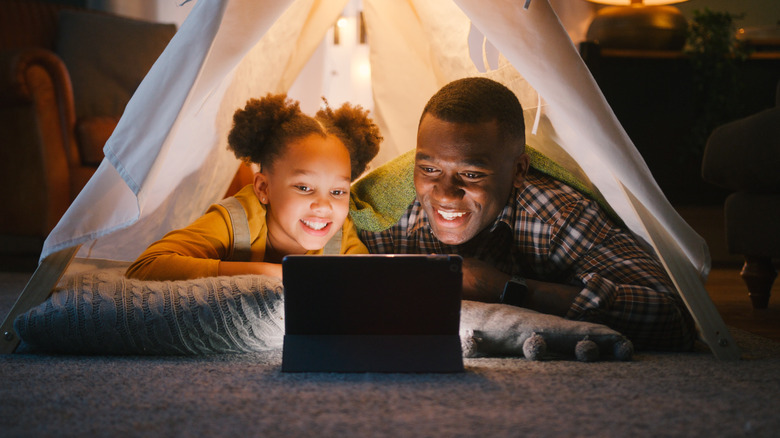 Father and daughter watching a movie on a tablet in a tent