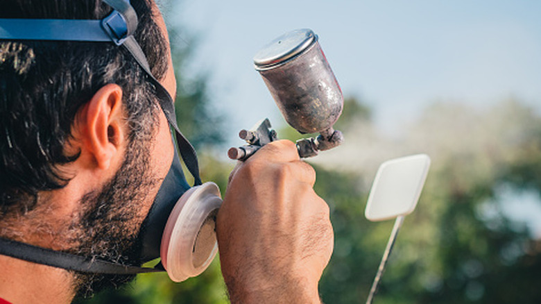 A person holding a stick to apply paint to a miniature object