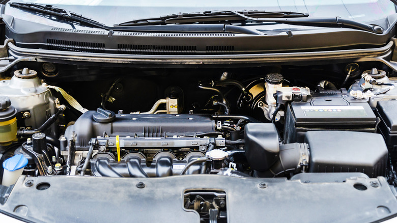 The inside of a car's engine bay with the engine, manifold, battery, and other components in view.