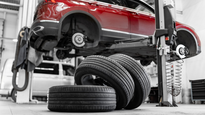 A red car jacked up in an auto shop with its tires removed and placed on the floor.
