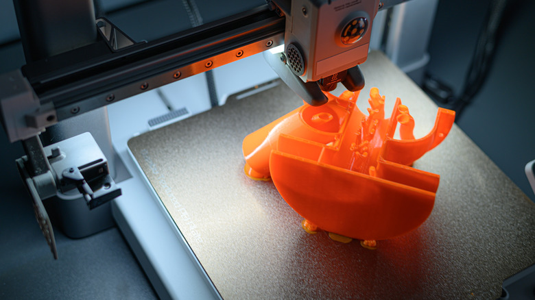 Active 3D printer creating a bright orange component.
