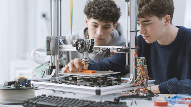 Young students working with a 3D printer placed on a tabletop.