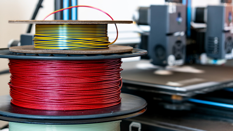 Spools of 3D printer filament stacked in various colors.