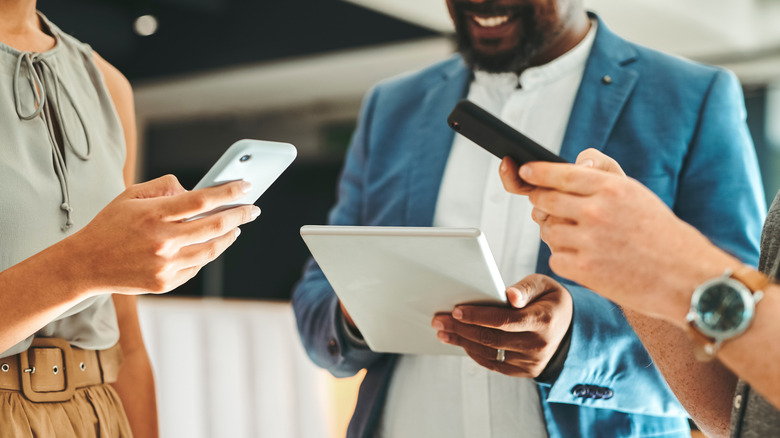 Three people standing besides one another using mobile devices.