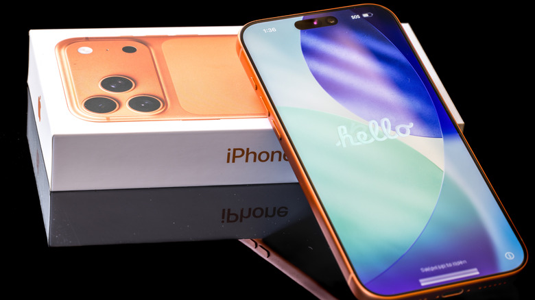 An iPhone 17 Pro Max in Cosmic Orange resting on its box, with a glossy white background