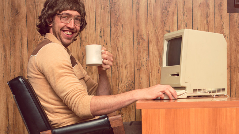 Man in retro '80s clothing and room using original Macintosh computer