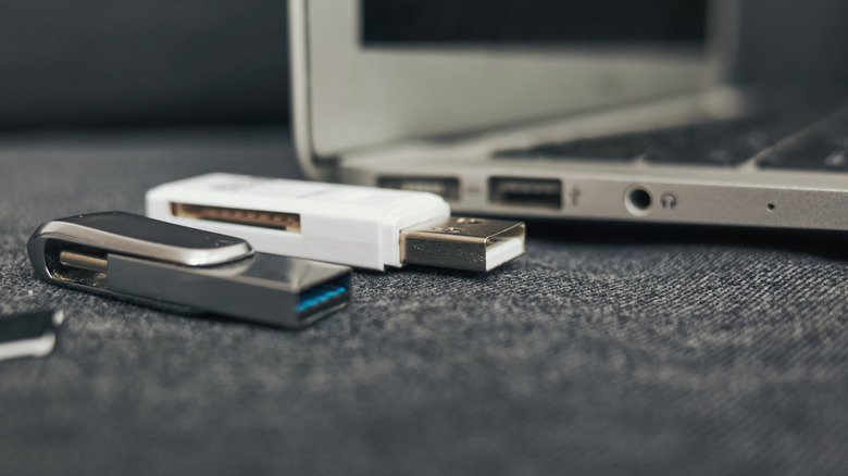 Several USB thumb drives next to a laptop.