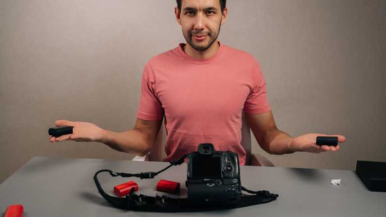 Person holding camera batteries in each hand while looking at the viewer.