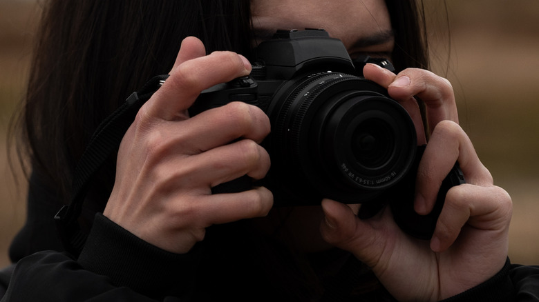 Photographer holding a mirrorless camera up to their face.