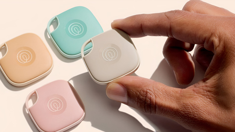 Hand holding a Life360 tile, while three other tiles are placed behind it