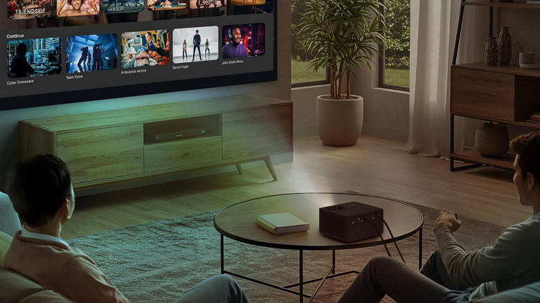 Two people watch as a Optoma PK31 Photon Life projects on image onto the wall