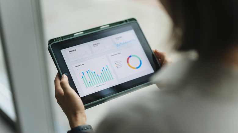 Person holding a tablet displaying business charts and graphs.