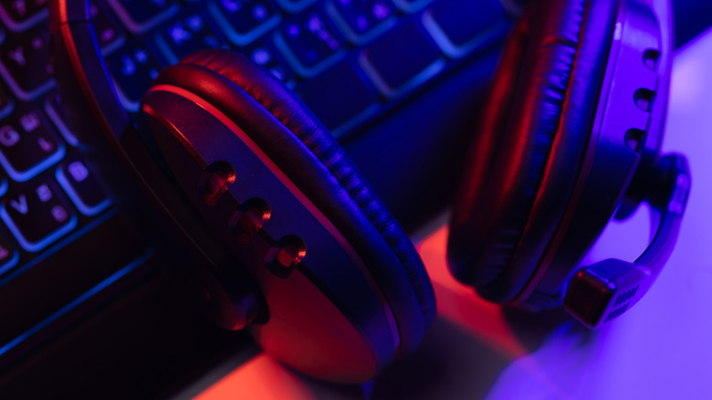 A closeup of a pair of black headphones with microphone sitting on top of a black, illuminated keyboard