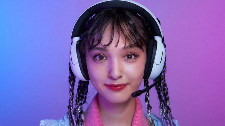 An individual wearing a pair of white Sony Inzone H5 wireless gaming headphones as they appear in front of a purple and blue backdrop