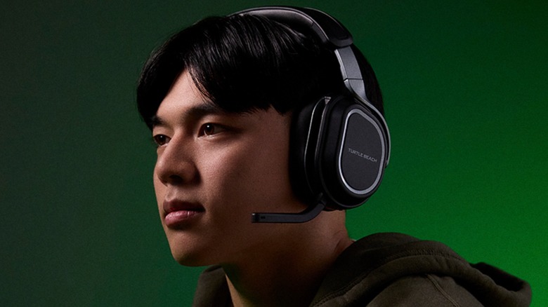 A user wearing a pair of black Turtle Beach 700 wireless headphones, the user is wearing a hoodie and is against a black and green background