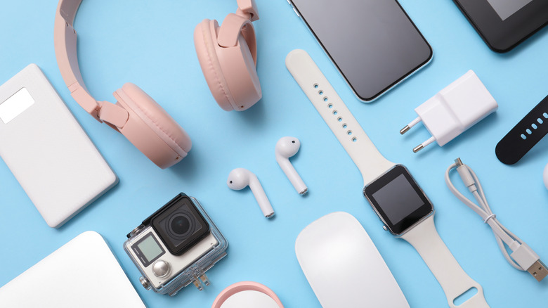 Various tech accessories, including smartphones, headphones, earbuds, a smartwatch, charger, cables, and action camera on a blue background.