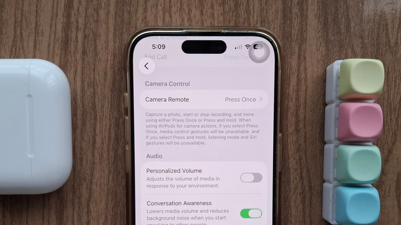 An iPhone showing the Camera Remote AirPods setting, next to an AirPods case and a fidget