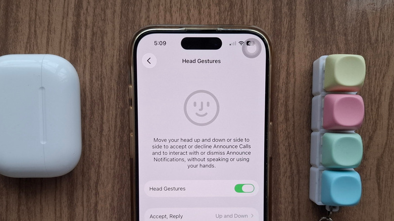 An iPhone showing the Head Gestures AirPods setting, next to an AirPods case and a fidget