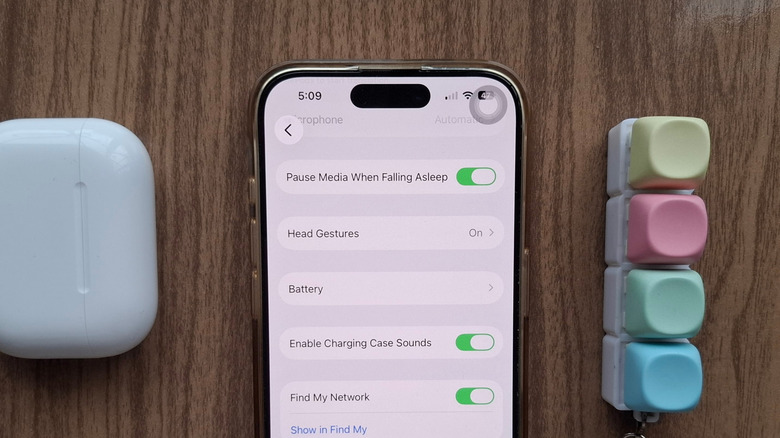 An iPhone showing the Pause Media When Falling Asleep AirPods setting, next to an AirPods case and a fidget