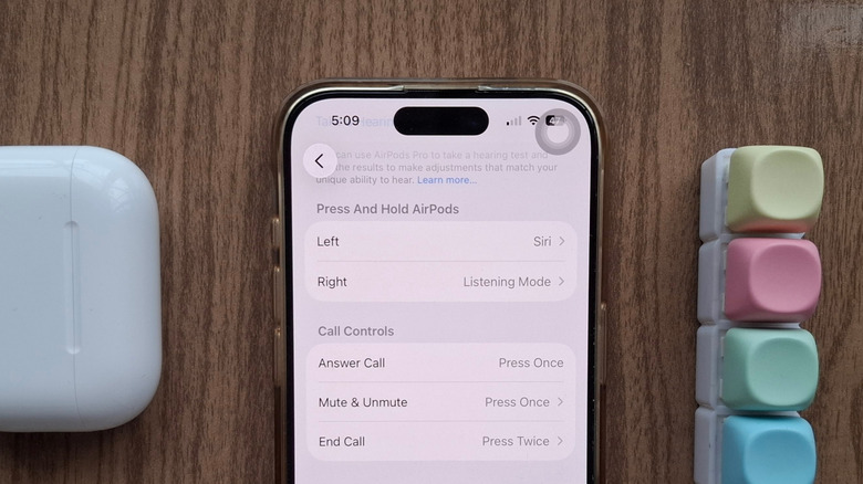 An iPhone showing the Siri activation AirPods setting, next to an AirPods case and a fidget