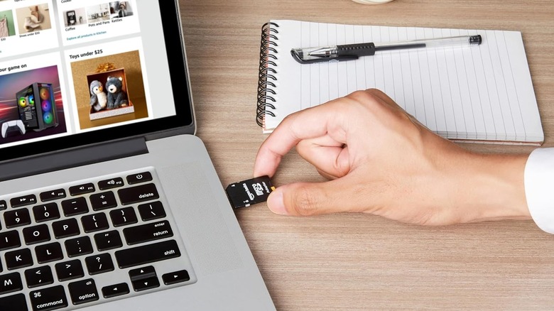 A hand inserting an Amazon Basics microSD card in an adapter into a laptop.