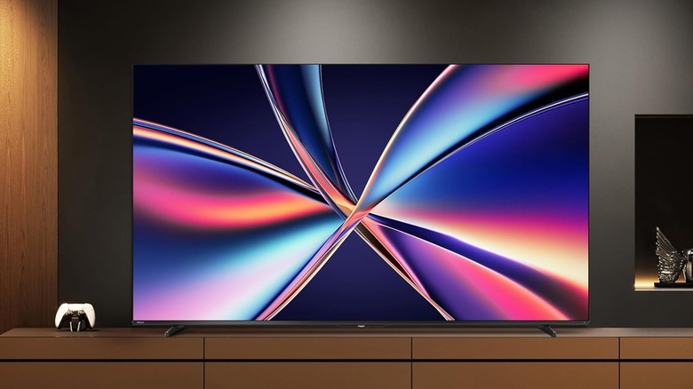 The Hisense 55-inch Cinema Series Hi-QLED 4K UHD Smart TV sitting atop of a TV stand with a controller is next to the TV