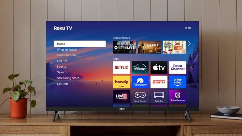 The Roku Select Series Smart TV sitting atop a TV stand displaying the Roku TV home screen