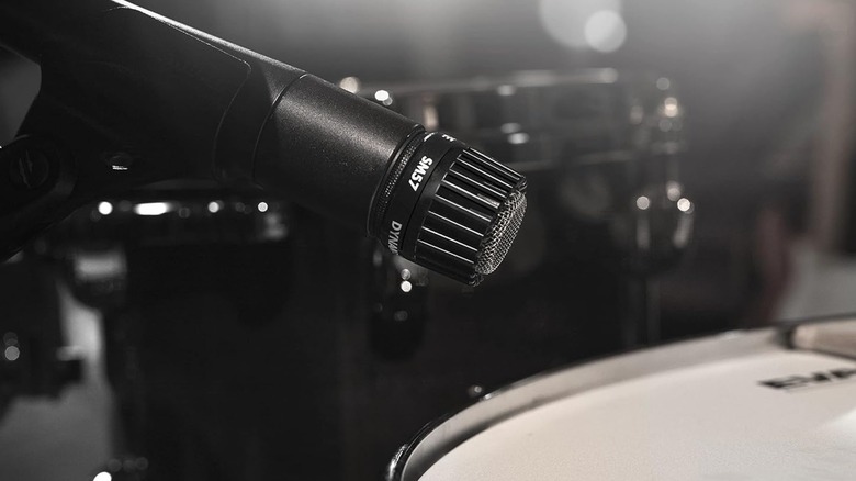 A black Shure SM57 Pro XLR Dynamic Instrument Microphone attached to a microphone stand as it mics a snare drum