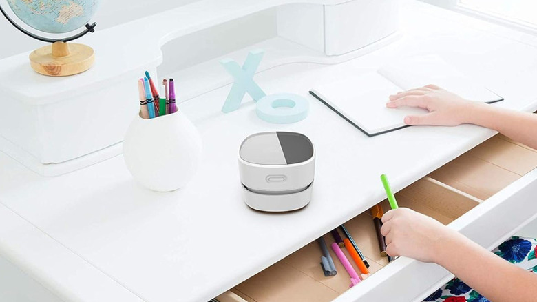 A Odistar Desktop Vacuum Cleaner on a white desk, with a person's hands nearby