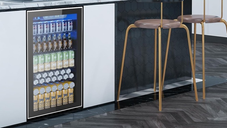 The Electactic 130-Can Beverage Mini Fridge installed under a counter, the fridge is next to two gold chairs