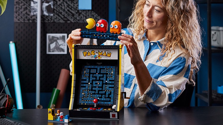 An individual in a white and blue striped shirt is putting the finishing touches on the LEGO Icons "Pac-Man" Arcade Building Set, specifically, they are setting the top of the set onto itself