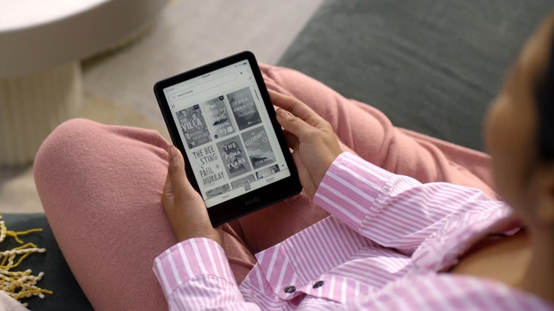 A woman holding the Amazon Kindle Paperwhite, which is on the library screen.