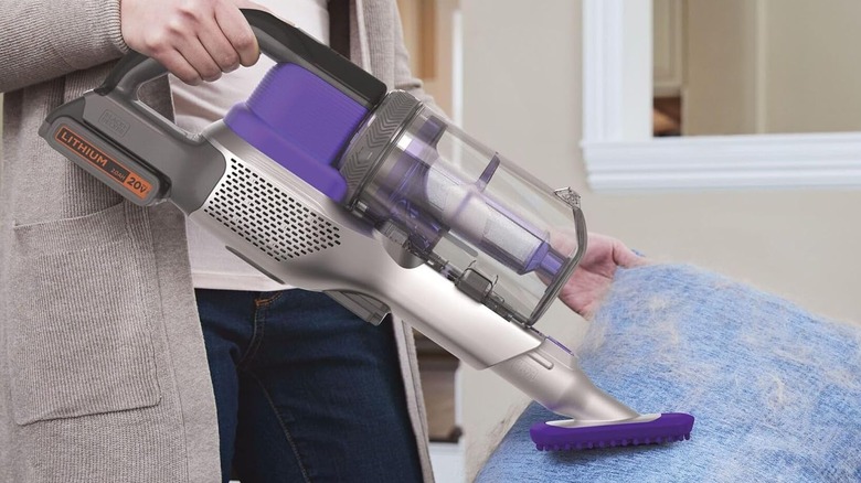 A person using the BLACK+DECKER POWERSERIES Extreme Pet 20V MAX cordless vacuum in handheld mode on a fur-covered pillow.