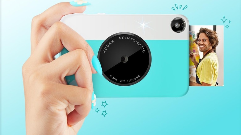 A hand holding the Kodak Printomatic instant camera, which is printing a photo.