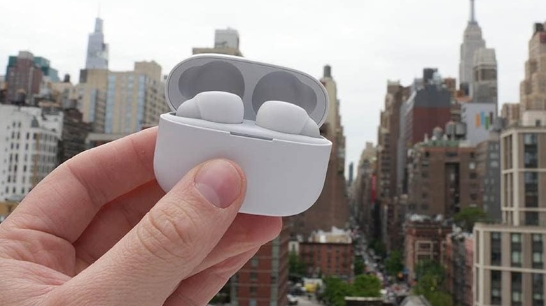 A hand holding the Sony LinkBuds S wireless earbuds outdoors while in their charging case.