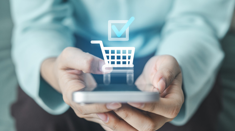 Shopping cart icon with a check mark hovering digitally above a smartphone.