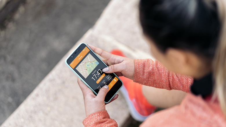 Unrecognized active woman with sports clothes using her mobile phone and checking her workout.