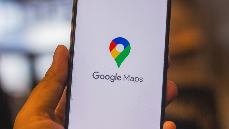 A person holding up a phone displaying Google Maps logo on a white background