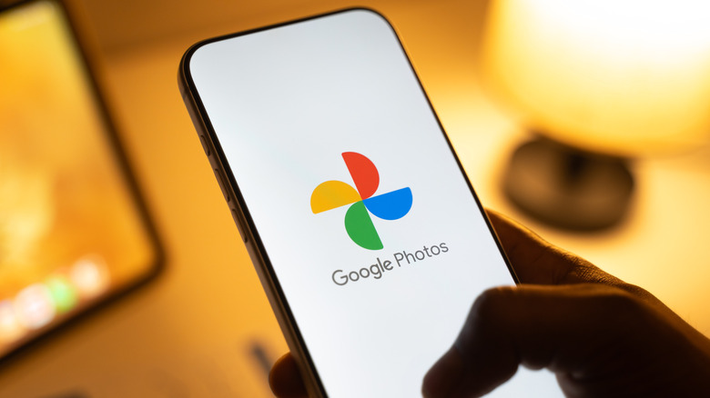 a person holding a smartphone showing the Google Photos logo over a white background