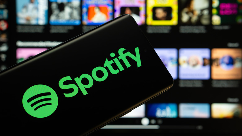A smartphone displayed in front of a screen showing the Spotify logo on a black background