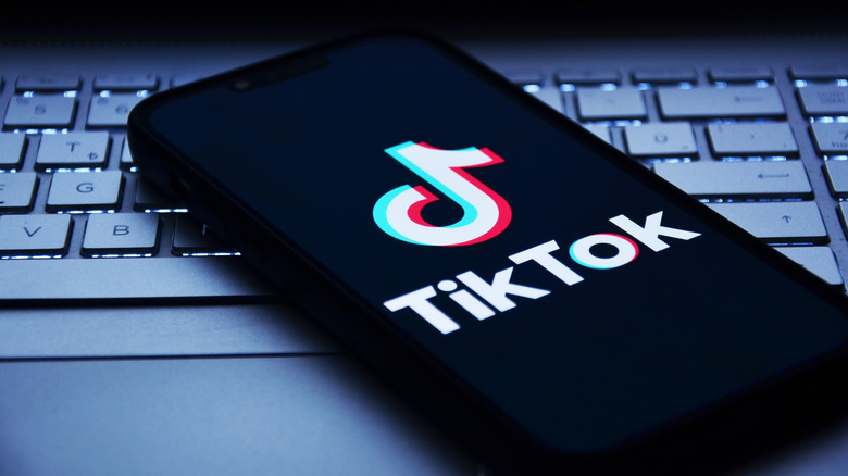 A phone sitting on a keyboard with the TikTok logo enlarged on its screen