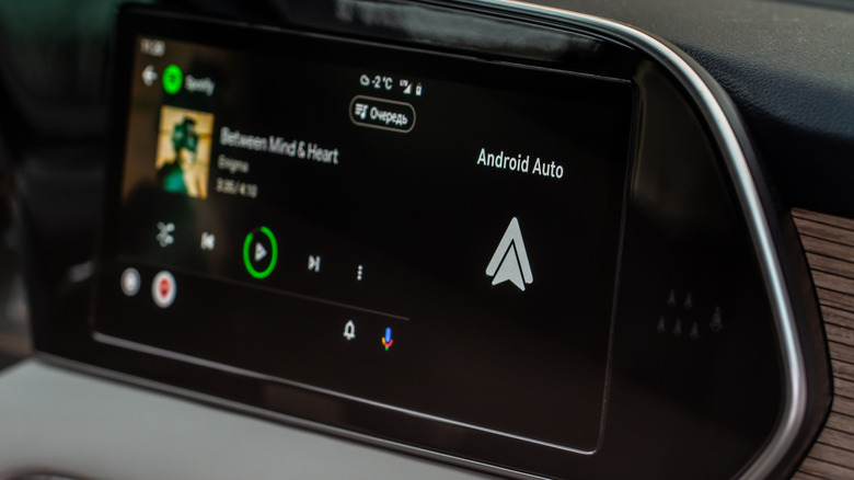 The Android Auto logo appears next to some audio playback controls. the display itself is within the dashboard of a vehicle