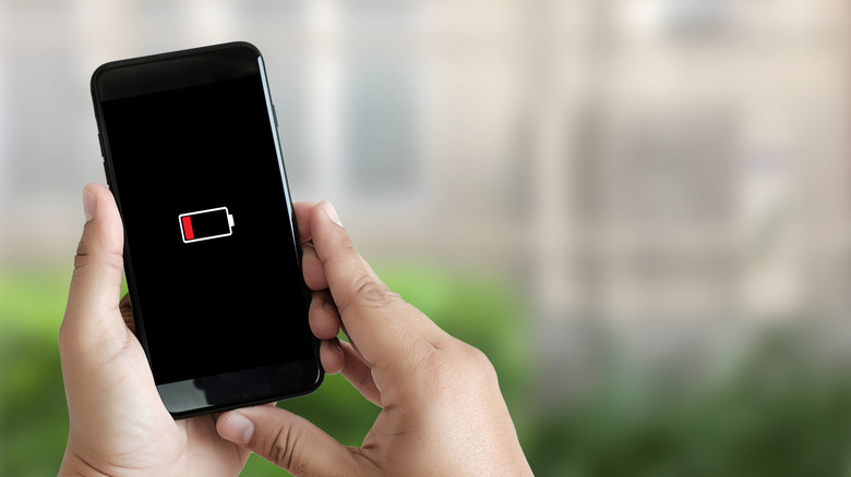 A person holding a phone with both their hands while the phone displays a low battery symbol on the screen
