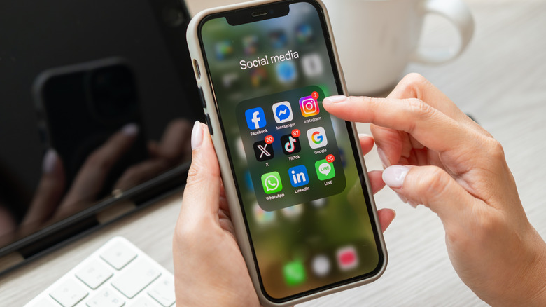 A folder including various social media apps open on a phone with a woman hovering her finger over them