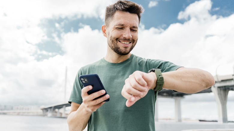 A man smiling as he looks at his watch while holding a phone in his other hand