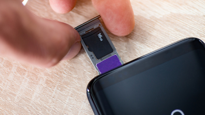 A hand is has two fingers around a microSD card holder that is getting ready to go into a smartphone