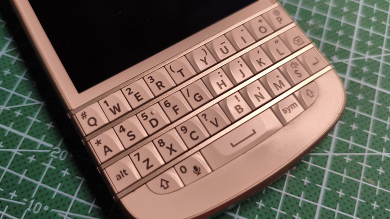 A pink smartphone with a full QWERTY keyboard,the phone is laying on a green, lined backdrop