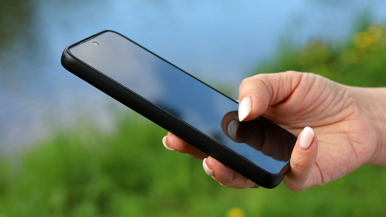 Close-up of a person holding a phone outdoor with blurred greenery in the background