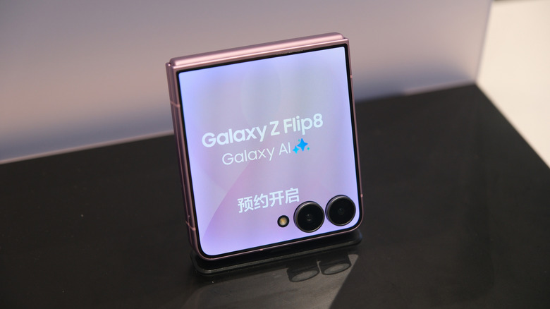 Samsung Galaxy Z Flip8 standing on a display stand with its cover screen and rear cameras visible.